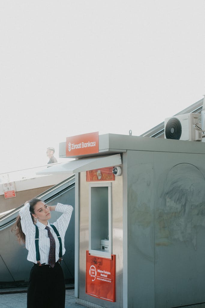 Young woman in formal attire near Ziraat Bank ATM, outdoor setting with bright sunlight.